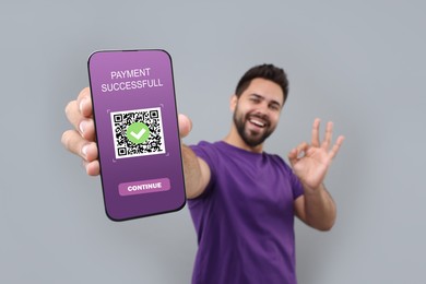 Image of Happy man showing Ok gesture and mobile phone with online payment application screen on grey background
