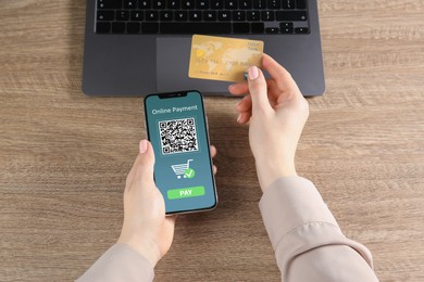 Woman using online payment application on mobile phone at table, top view