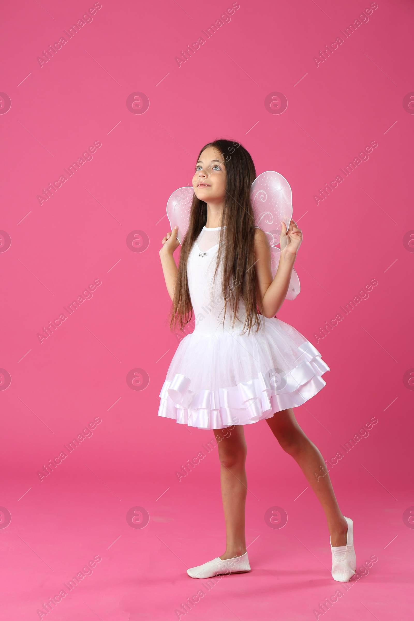 Photo of Cute little girl in fairy costume with white wings on pink background