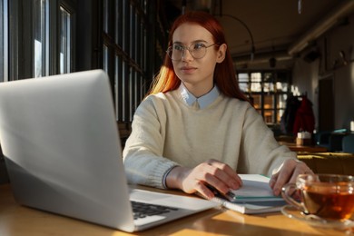 Photo of Young female student with laptop studying at table in cafe