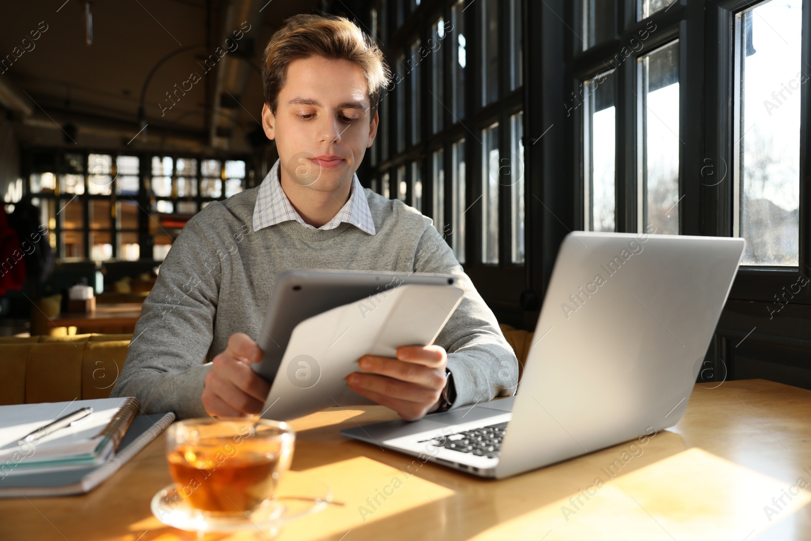 Photo of Teenage student with laptop and tablet studying at table in cafe