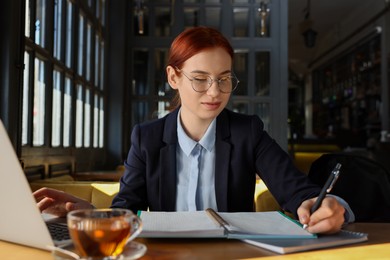 Photo of Young female student with laptop studying at table in cafe