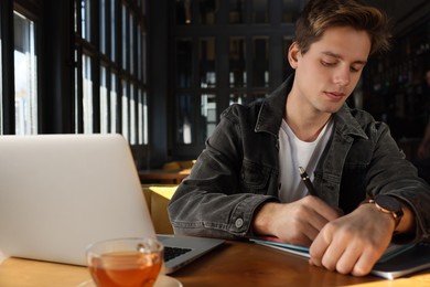 Photo of Teenage student with laptop studying at table in cafe