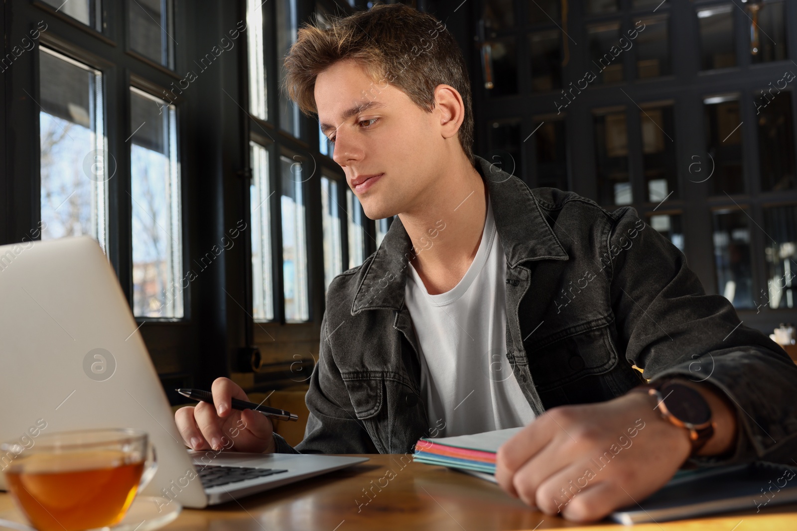 Photo of Teenage student with laptop studying at table in cafe