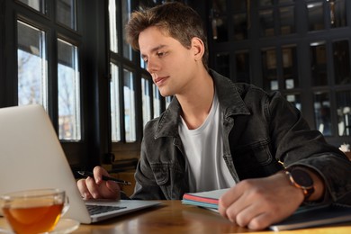 Photo of Teenage student with laptop studying at table in cafe