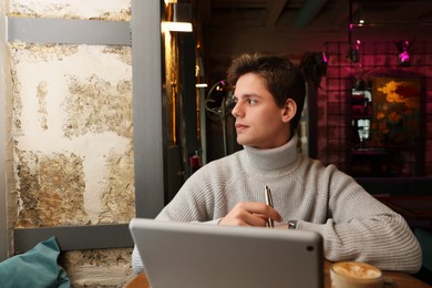 Photo of Teenage student with tablet studying at table in cafe