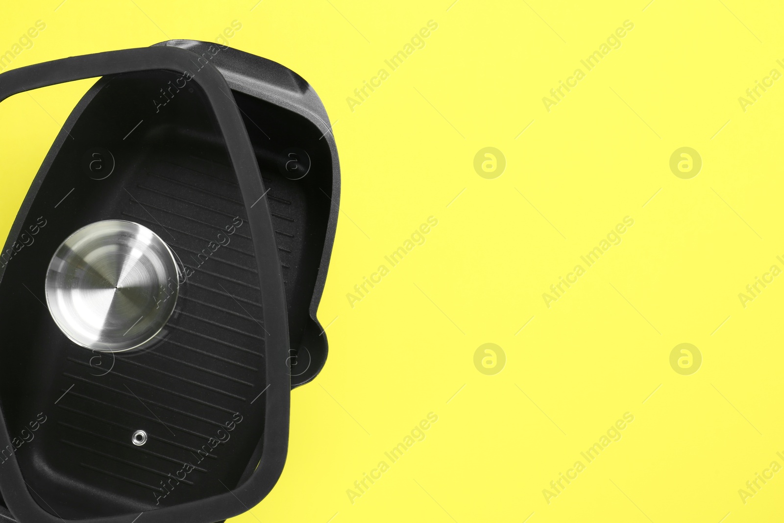 Photo of Black pot with glass lid on yellow background, top view. Space for text