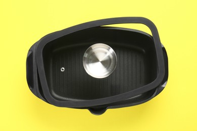 Photo of Black pot with glass lid on yellow background, top view