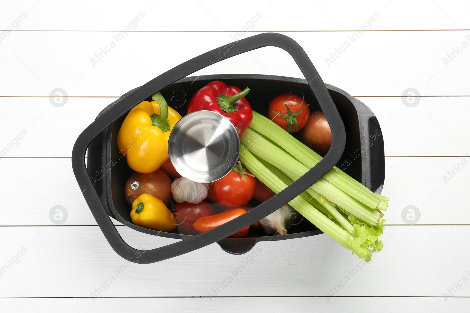 Photo of Black pot with fresh vegetables on white wooden table, top view