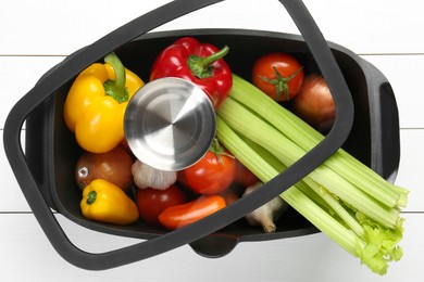 Photo of Black pot with fresh vegetables on white wooden table, top view