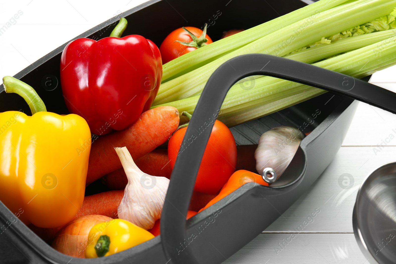 Photo of Black pot with fresh vegetables and glass lid on white wooden table