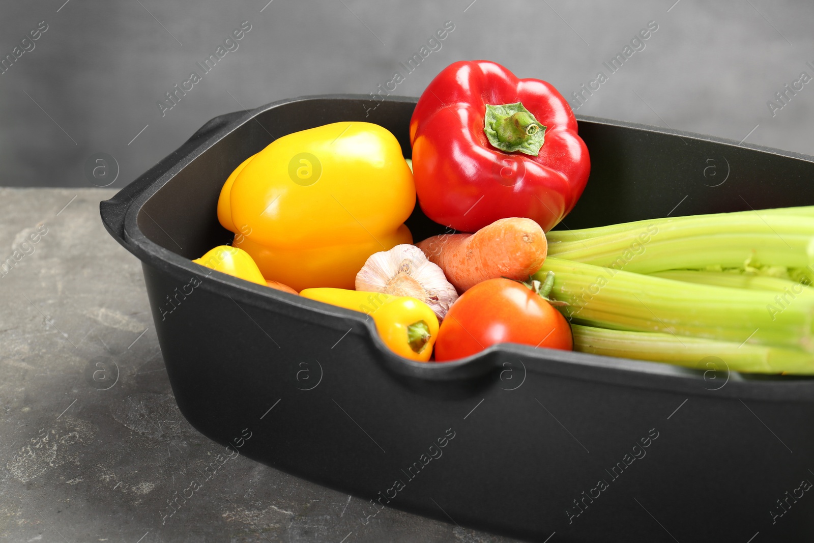 Photo of Black pot with fresh vegetables on grey table