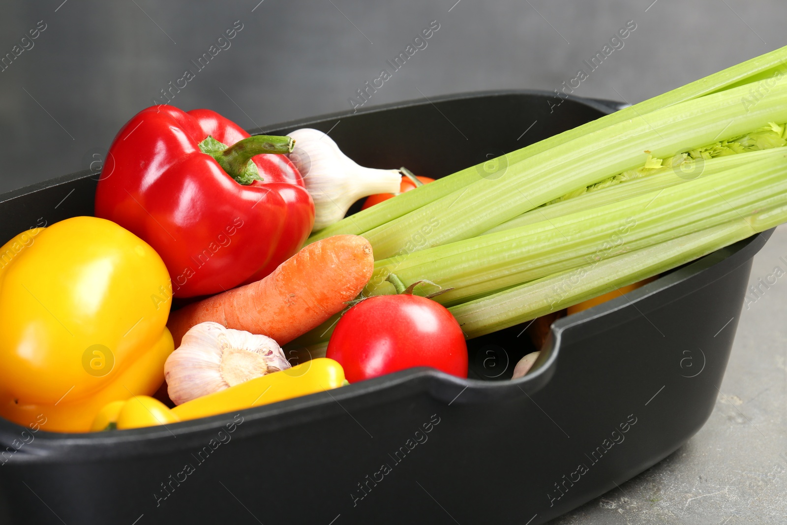 Photo of Black pot with fresh vegetables on grey table