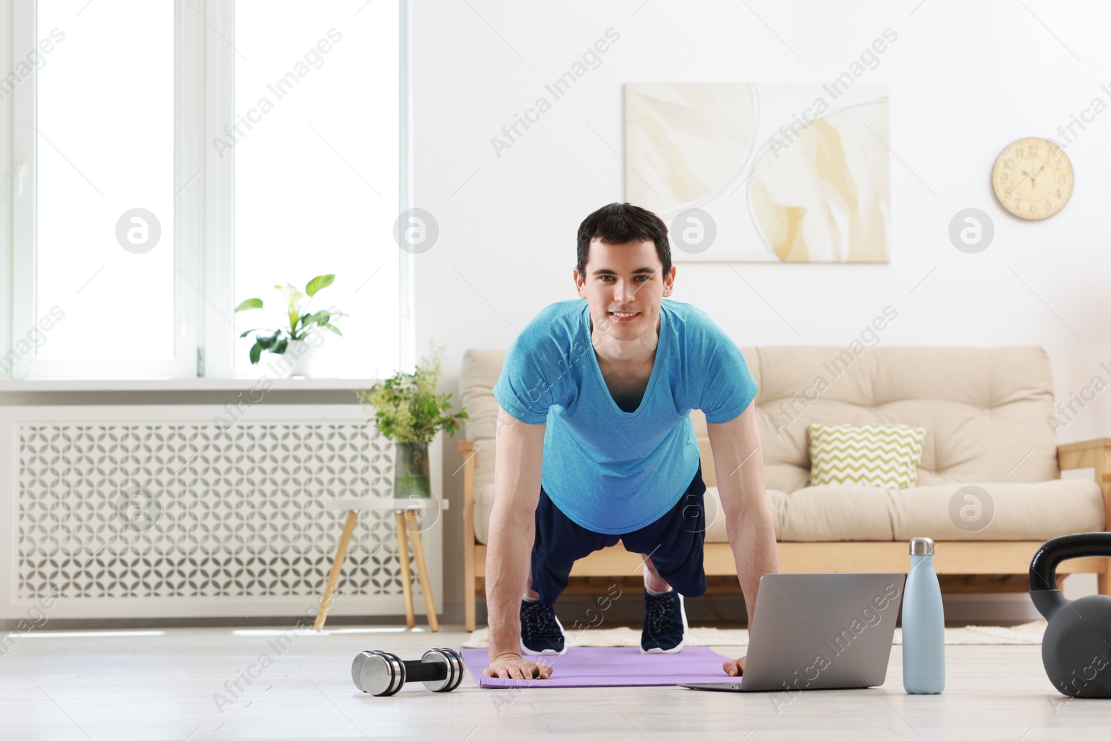 Photo of Online fitness trainer. Man doing exercise near laptop at home