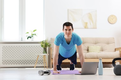 Online fitness trainer. Man doing exercise near laptop at home