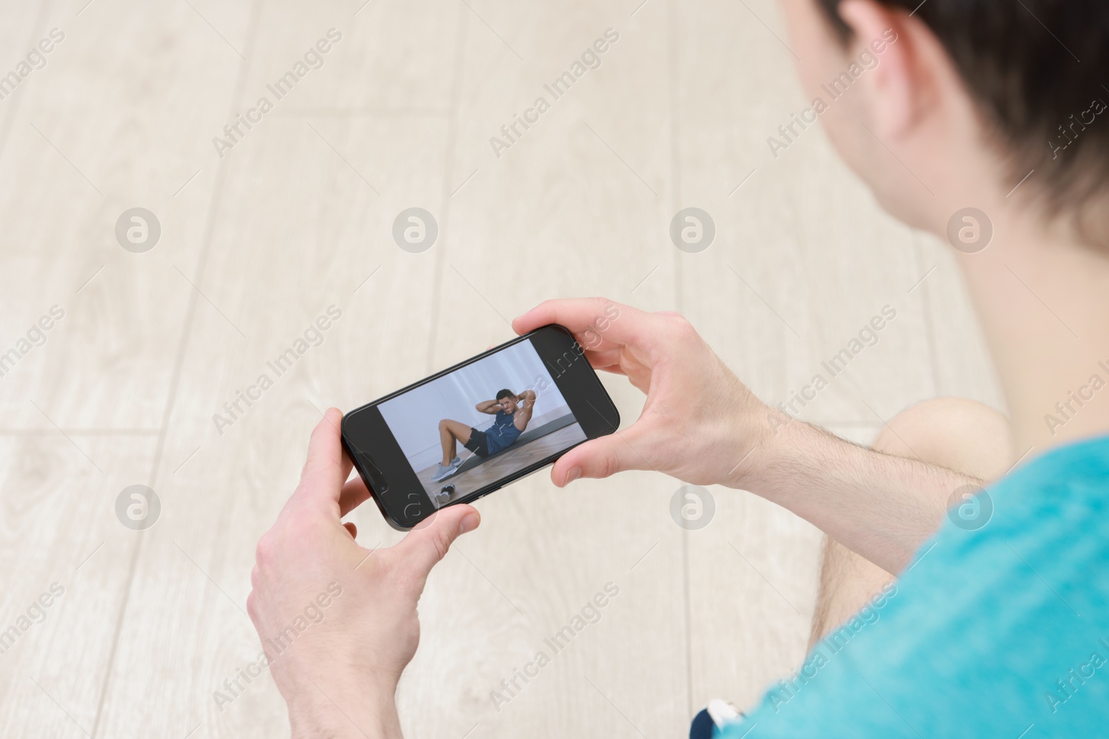 Photo of Online fitness trainer. Man watching tutorial on smartphone indoors, closeup