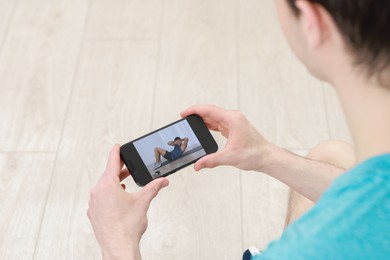 Photo of Online fitness trainer. Man watching tutorial on smartphone indoors, closeup