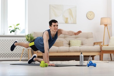 Photo of Online fitness trainer. Man doing exercise near laptop at home