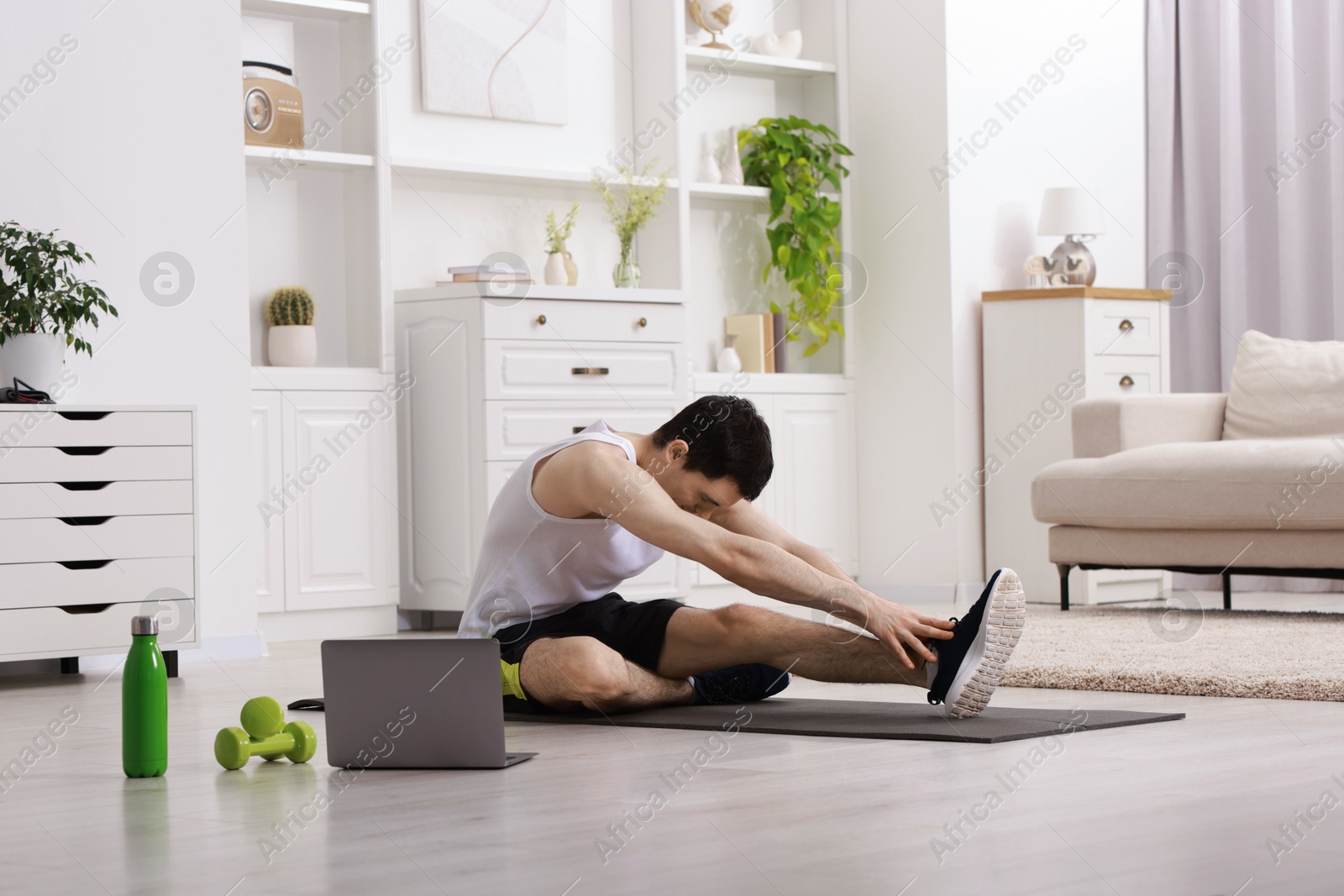 Photo of Online fitness trainer. Man doing exercise near laptop at home