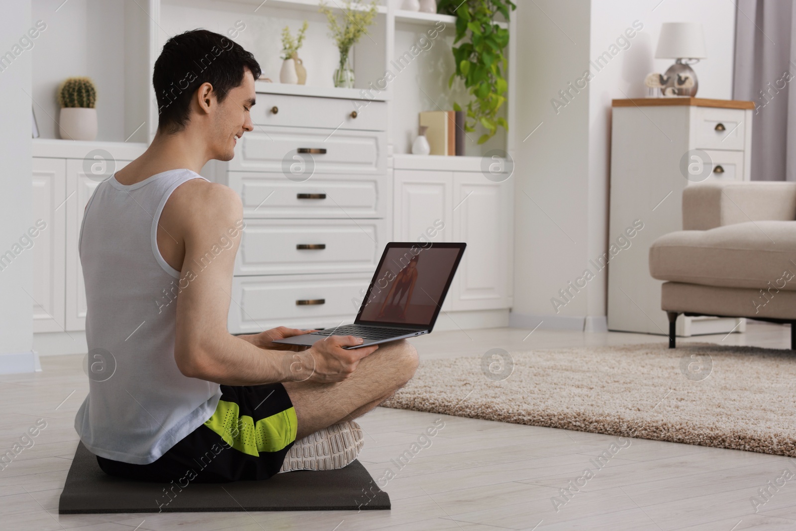 Photo of Online fitness trainer. Man watching tutorial on laptop indoors