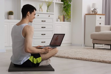 Online fitness trainer. Man watching tutorial on laptop indoors