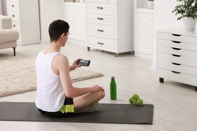 Photo of Online fitness trainer. Man watching tutorial on smartphone at home