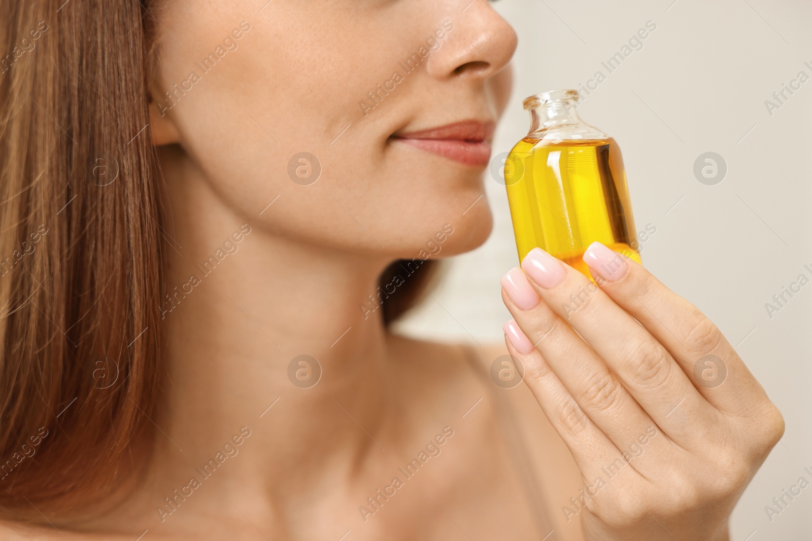 Photo of Aromatherapy. Woman with bottle of essential oil on light background, closeup