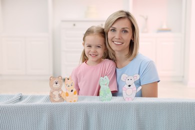 Family portrait of smiling mother and daughter performing show at home. Puppet theatre