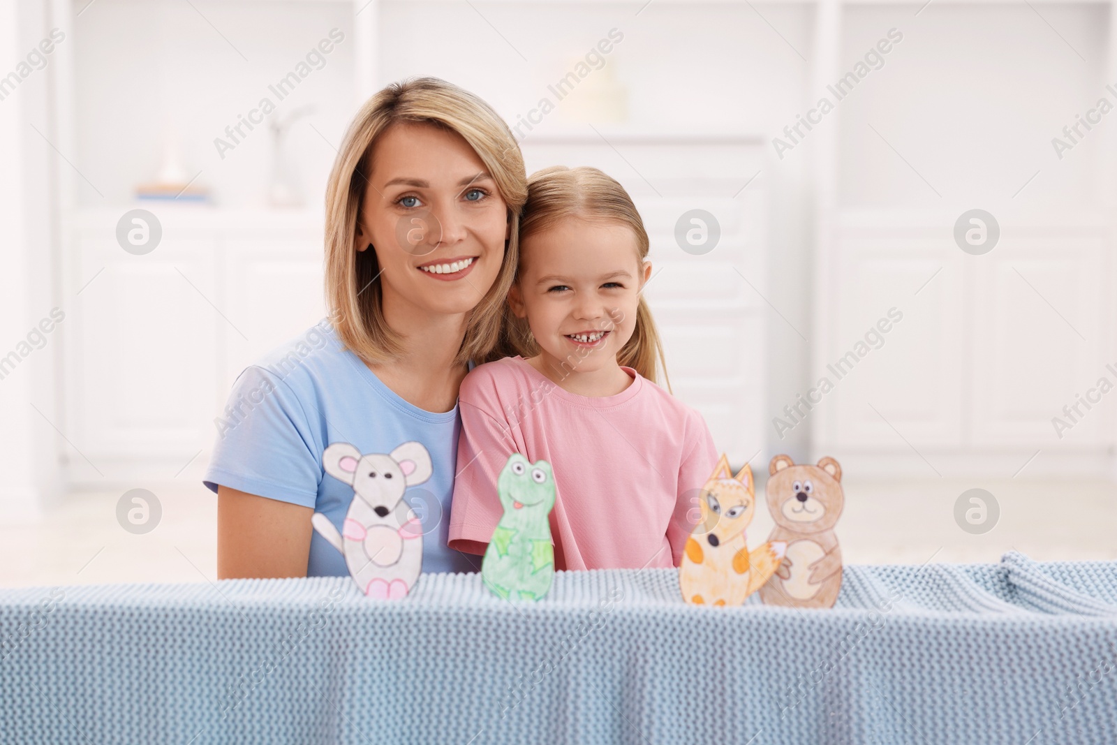 Photo of Family portrait of smiling mother and daughter performing show at home. Puppet theatre