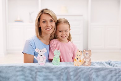 Photo of Family portrait of smiling mother and daughter performing show at home. Puppet theatre