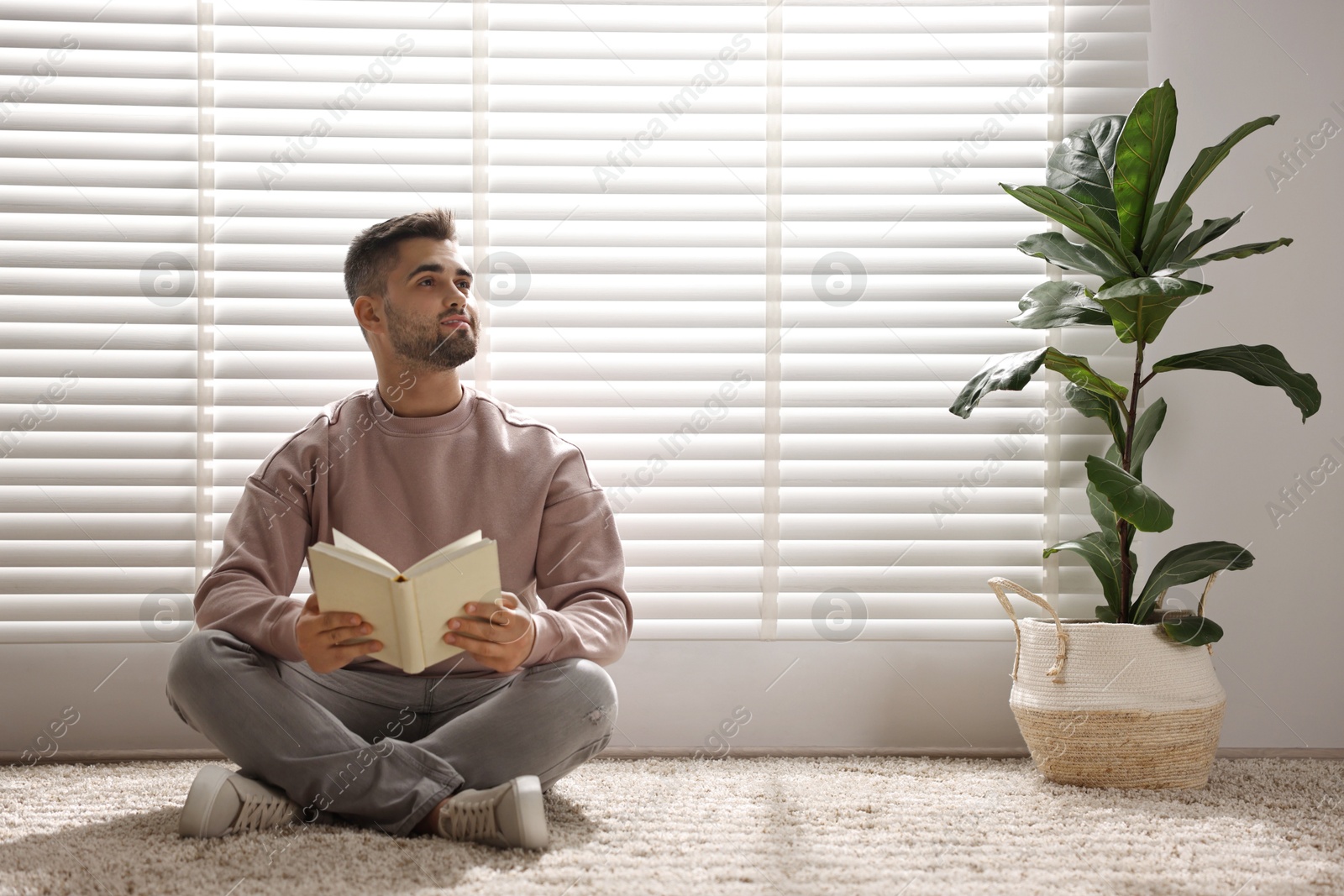 Photo of Man reading book near window blinds at home