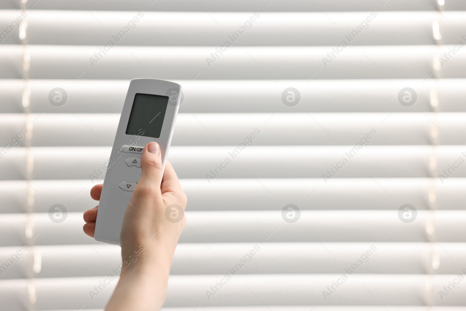 Photo of Woman using remote control to adjust window blinds indoors, closeup. Space for text