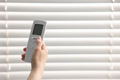 Woman using remote control to adjust window blinds indoors, closeup. Space for text