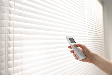 Photo of Woman using remote control to adjust window blinds indoors, closeup. Space for text