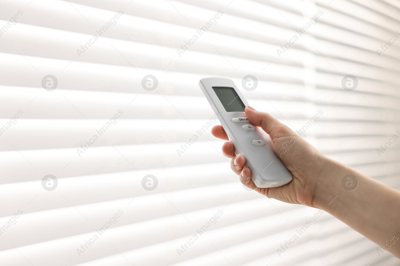 Photo of Woman using remote control to adjust window blinds indoors, closeup. Space for text