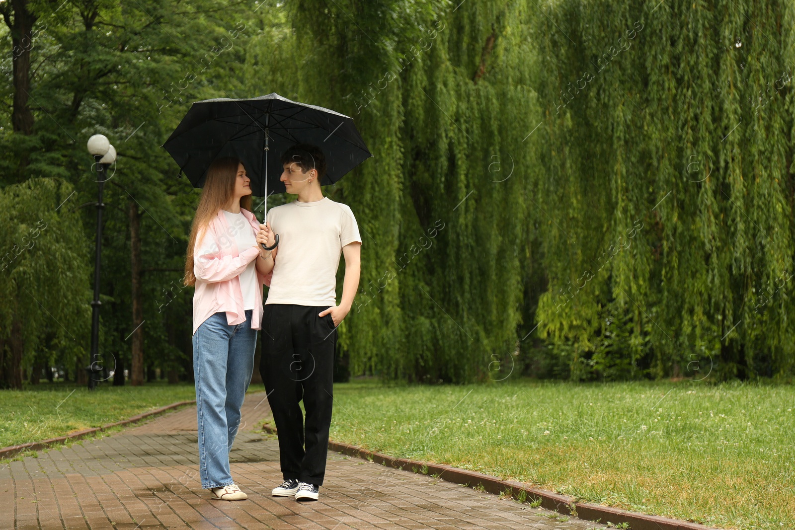 Photo of International dating. Lovely young couple with umbrella spending time together in park, space for text