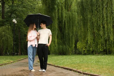 International dating. Lovely young couple with umbrella spending time together in park, space for text
