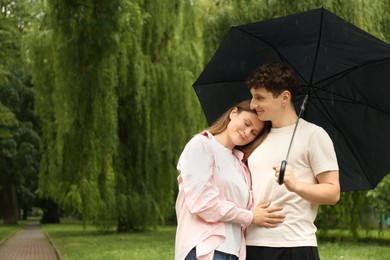 Photo of International dating. Lovely young couple with umbrella spending time together in park, space for text