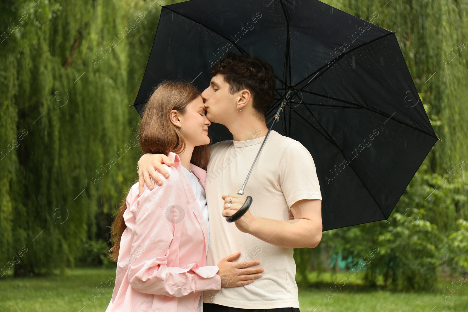 Photo of International dating. Lovely young couple with umbrella spending time together in park