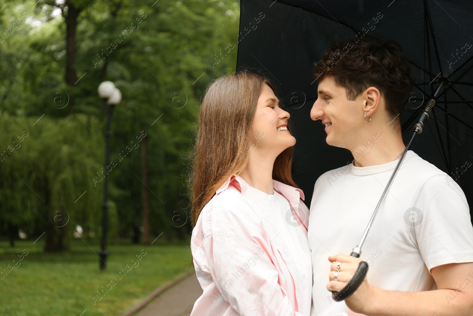 Photo of International dating. Lovely young couple with umbrella spending time together in park, space for text