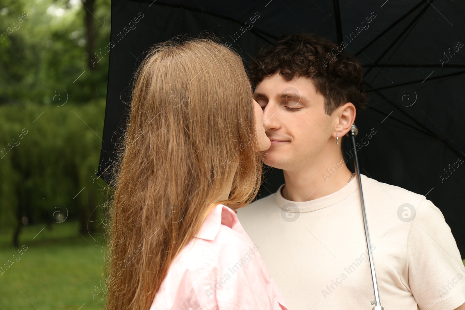 Photo of International dating. Lovely young couple with umbrella spending time together in park