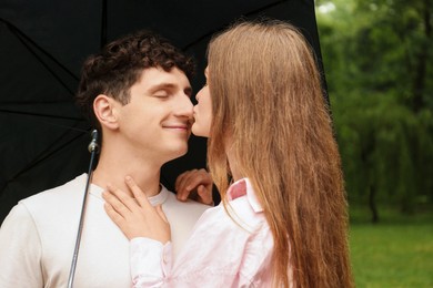 Photo of International dating. Lovely young couple with umbrella spending time together in park