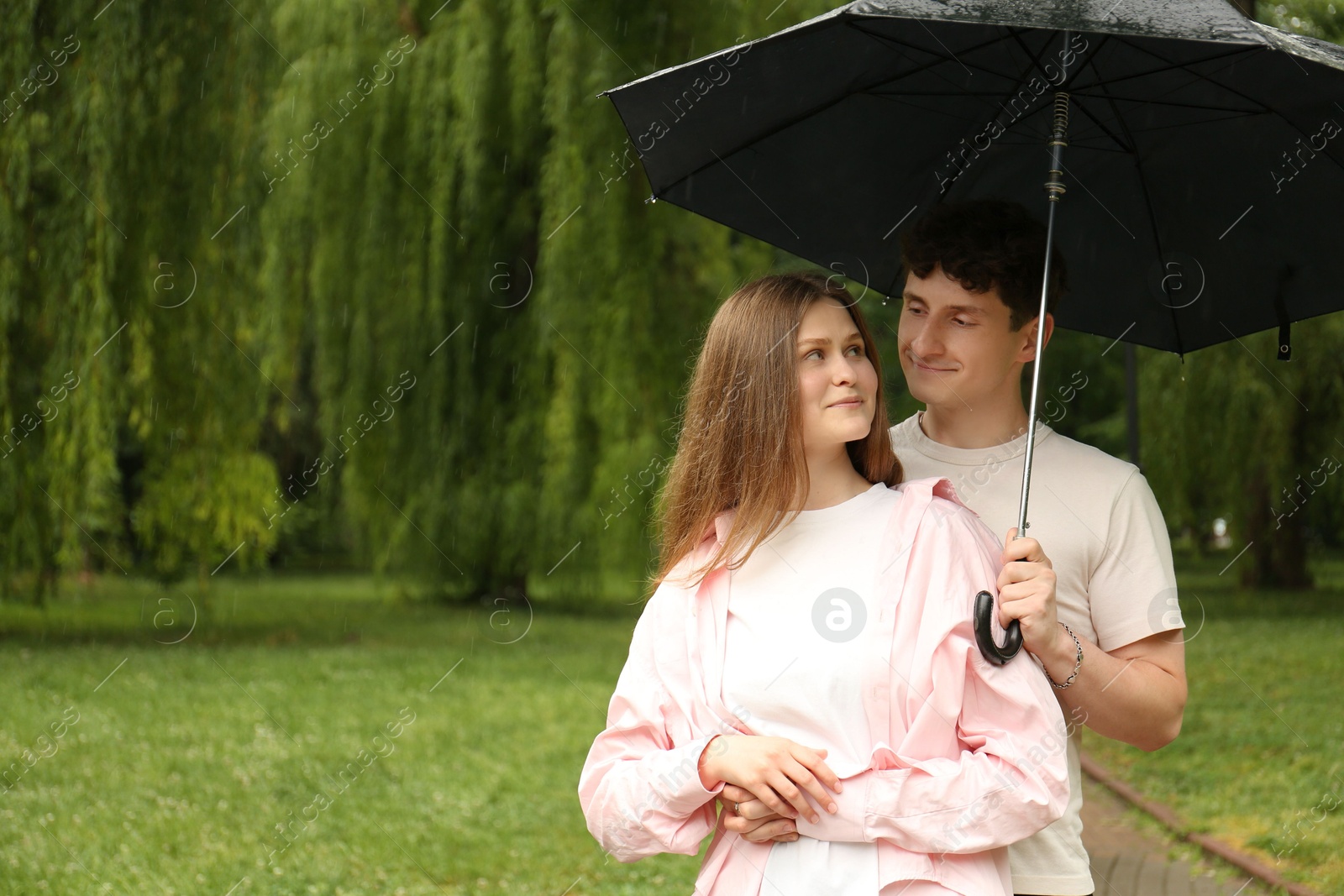 Photo of International dating. Lovely young couple with umbrella spending time together in park, space for text