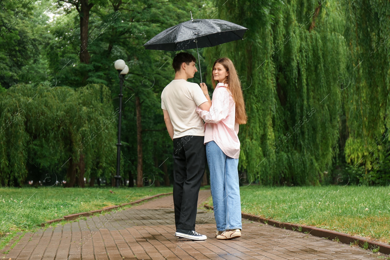 Photo of International dating. Lovely young couple with umbrella spending time together in park