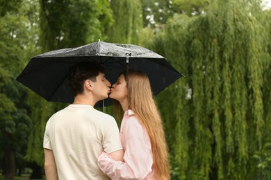 Photo of International dating. Lovely young couple with umbrella spending time together in park