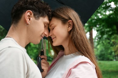 Photo of International dating. Lovely young couple with umbrella spending time together in park