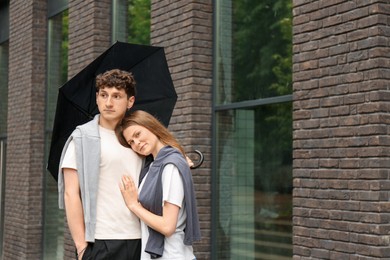 Photo of International dating. Lovely young couple with umbrella spending time together outdoors, space for text