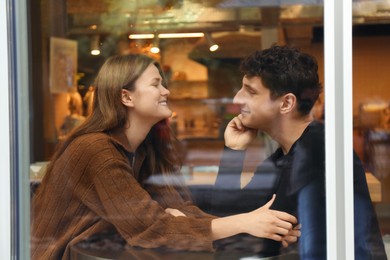 Photo of International dating. Lovely young couple spending time together in cafe, view through glass window