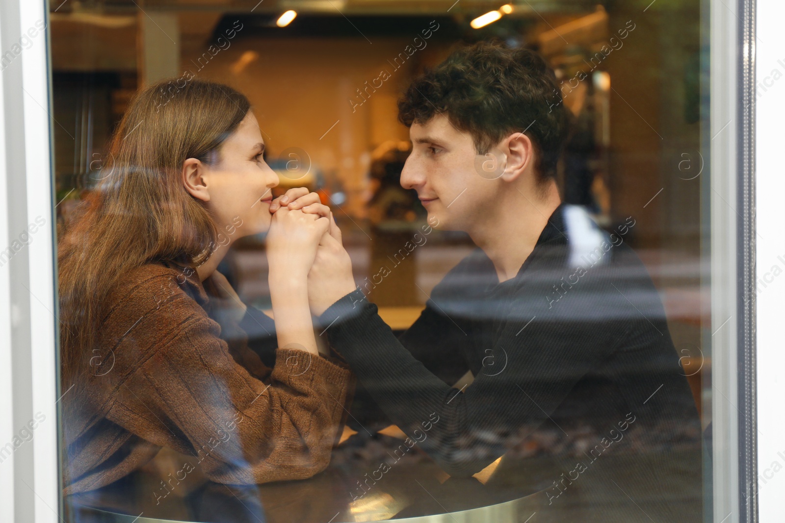 Photo of International dating. Lovely young couple spending time together in cafe, view through glass window