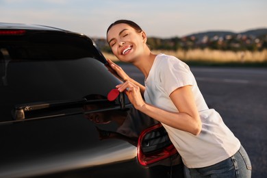 Happy young woman with key near her new car outdoors